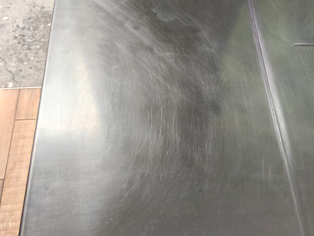 Tarja de acero inoxidable con rayones en remolino y manchas tras tallarla con el material equivocado